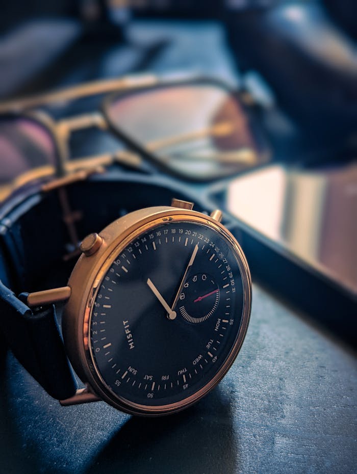 Elegant gold wristwatch with black dial and glasses in the background.